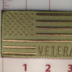 Green embroidered patch with the American flag and the word "VETERAN" in bold text, shown against a gridded background for scale.